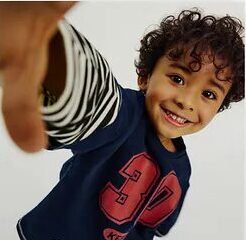 Child in an oversized blue outfit sitting in a playful fashion pose.